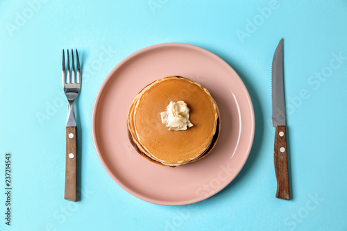 Plate with hot tasty pancakes and butter on color background