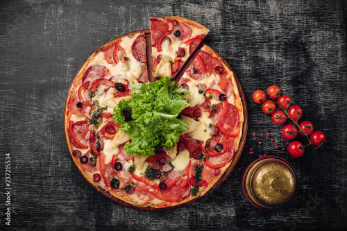 Pizza with ham, salami, cheese, mushrooms, cherry tomatoes, bell peppers and salad on a black chalk board, top view.