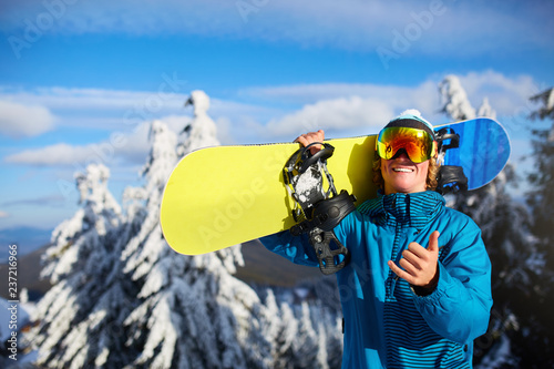 Photography Smiling snowboarder posing carrying snowboard on shoulders at ski resort near forest before freeride session