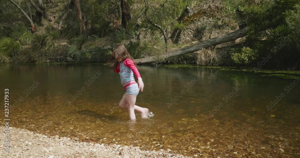 young girl playing in a river flicks water into an arch over her head and splashes ankle deep in the river young girl playing in a river flicks water into an arch over her head and splashes ankle deep in the river