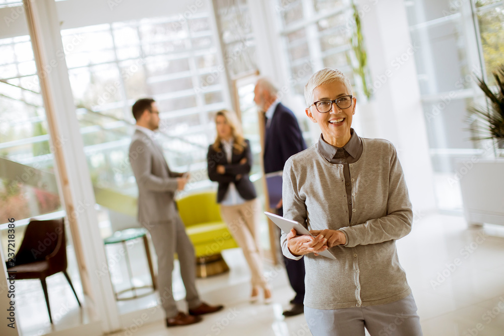 Portrait of senior businesswoman with digital tablet while other business people standing in background Portrait of senior businesswoman with digital tablet while other business people standing in background