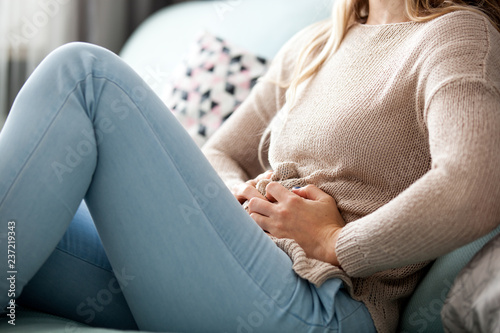 Young woman suffering from abdominal pain while sitting on sofa at home photo