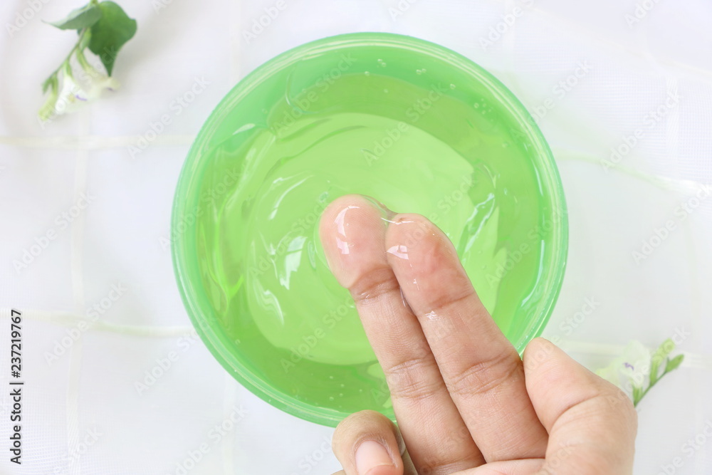 Top view of close up woman finger applying aloe vera gel cream in green container on white fabric background Top view of close up woman finger applying aloe vera gel cream in green container on white fabric background
