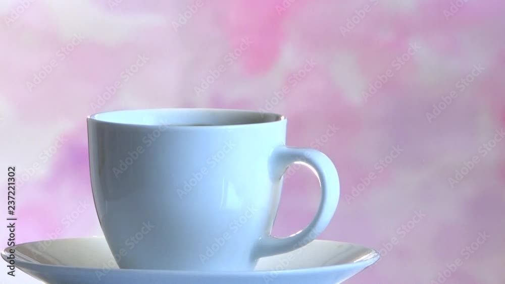 Pouring coffee into a white cup on a plate on a pink background Pouring coffee into a white cup on a plate on a pink background
