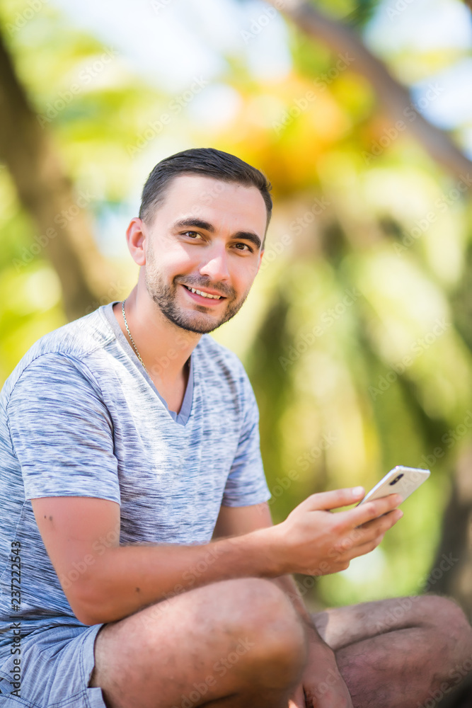 Casual happy man typing on smartphone sitting on a bench in a park Casual happy man typing on smartphone sitting on a bench in a park