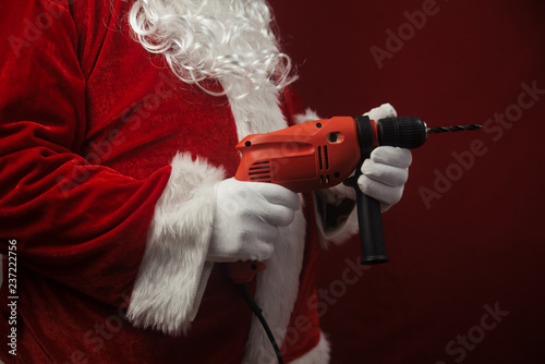Santa Claus holding using electric drill ready to renovate space background. Handyman repairman in festive mood for seasonal business work. Merry Christmas and Happy New Year time.