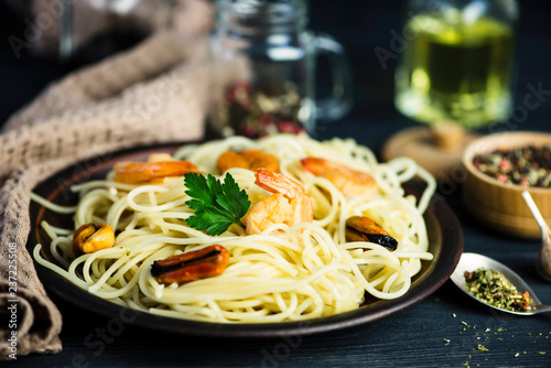 spaghetti with seafood in a plate and spices on a wooden board