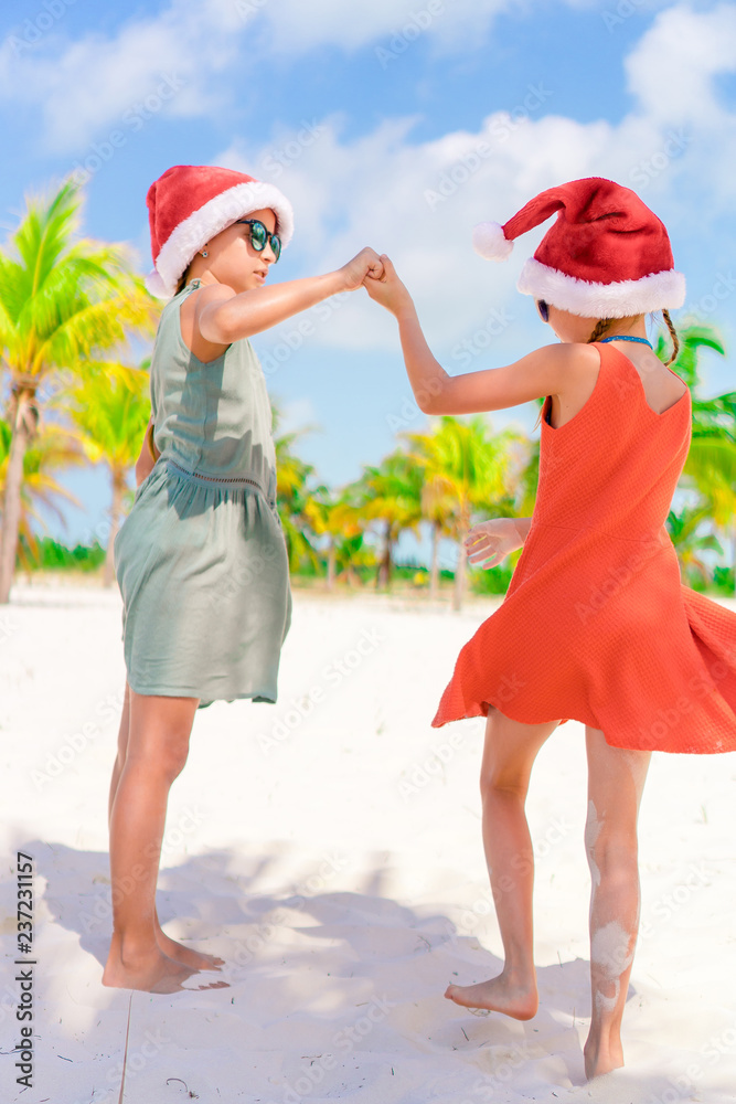 Obraz premium Little adorable girls in Santa hats during beach vacation have fun together