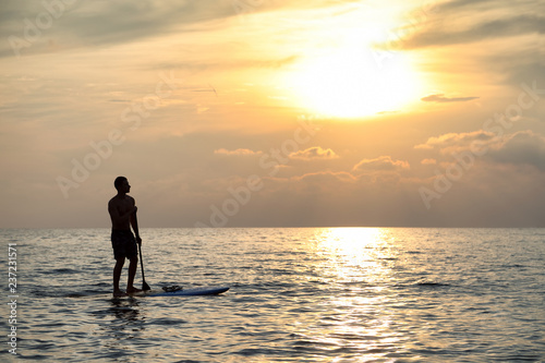 Sunset Silhouette Of Young Handsome Man Paddling On Surfboard Toward The Horizon In The Open Sea Beautiful Scenic Sunset © likstudio
