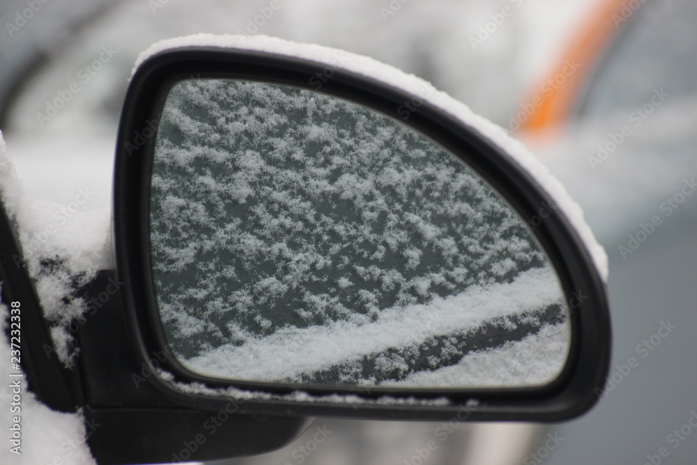 Light snow on the mirror of a silver car, reflected in the mirror. The first clean fluffy snow.