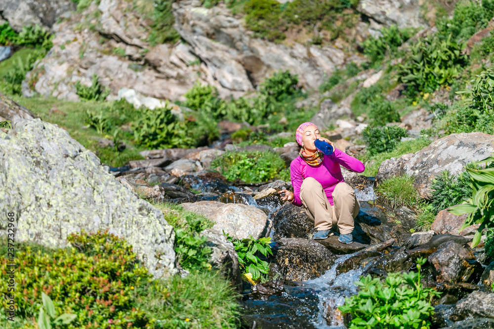 carefree woman hiker taking water from forest strean and drink it.