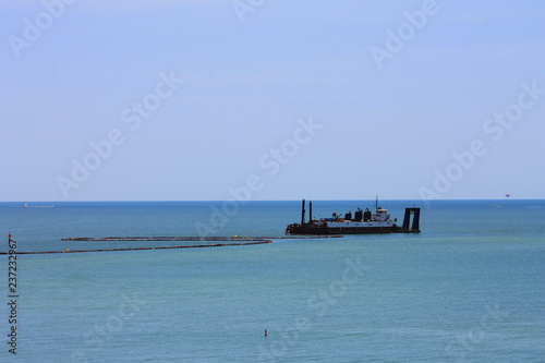 Ship with boom, in the Gulf of Mexico, Madeira Beach, Florida.  Ship is dredging sand from the sea floor. Lots of sky and water in image.