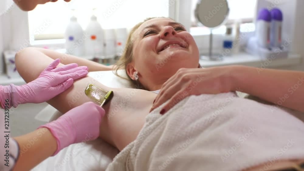 Beautician in a white robe makes waxing armpits. Fat girl in a beauty salon. The girl makes a depilation of the armpits. Beautician in a white robe makes waxing armpits. Fat girl in a beauty salon. The girl makes a depilation of the armpits.