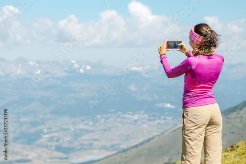 woman hiker taking photo with her smart phone on the top of the mountain peak