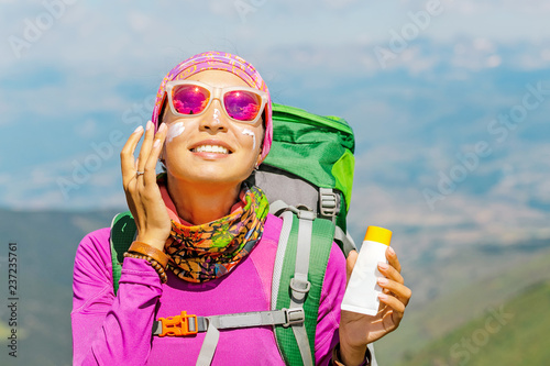 Hiker woman applying sun cream to protect her skin from dangerous uv sun rays high in mountains. Travel healthcare concept