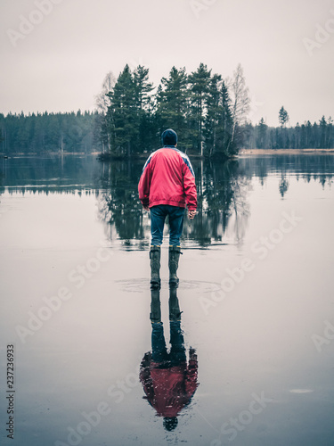 Man is walking on water ice lake. Light is reflected lika a mirror. Small island in background.