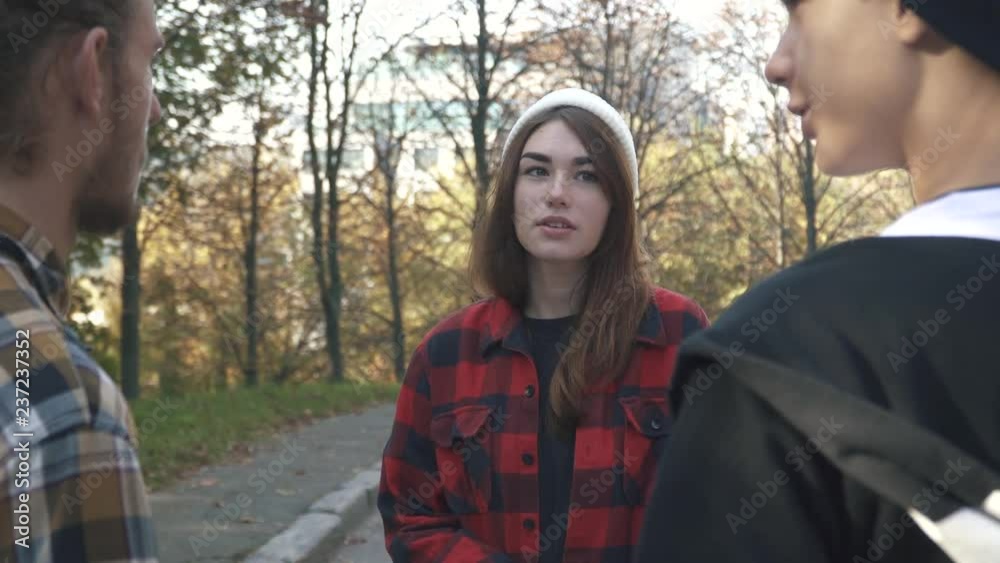 Friends chatting outdoors. The girl in the white hat and plaid shirt talking to two guys in the park.