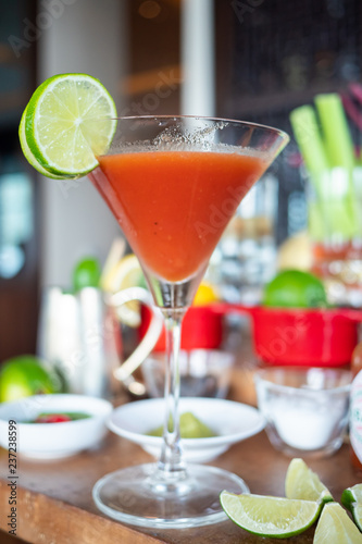 Fotografi Delicious Bloody Mary cocktail or tomato juice garnished with lime wedge in martini glass on a bar counter with ingredients background