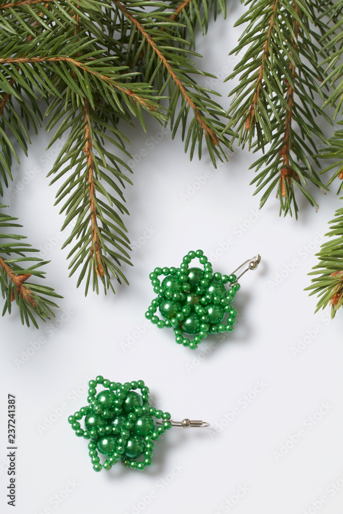 Women's earrings made of beads among the branches of spruce. On a white background.