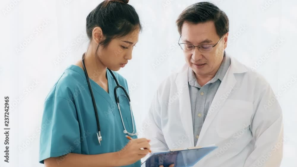 Senior asian man medical doctor harassing young medical doctor woman sitting on her desk. Young medical doctor office harassment concept. Senior asian man medical doctor harassing young medical doctor woman sitting on her desk. Young medical doctor office harassment concept.