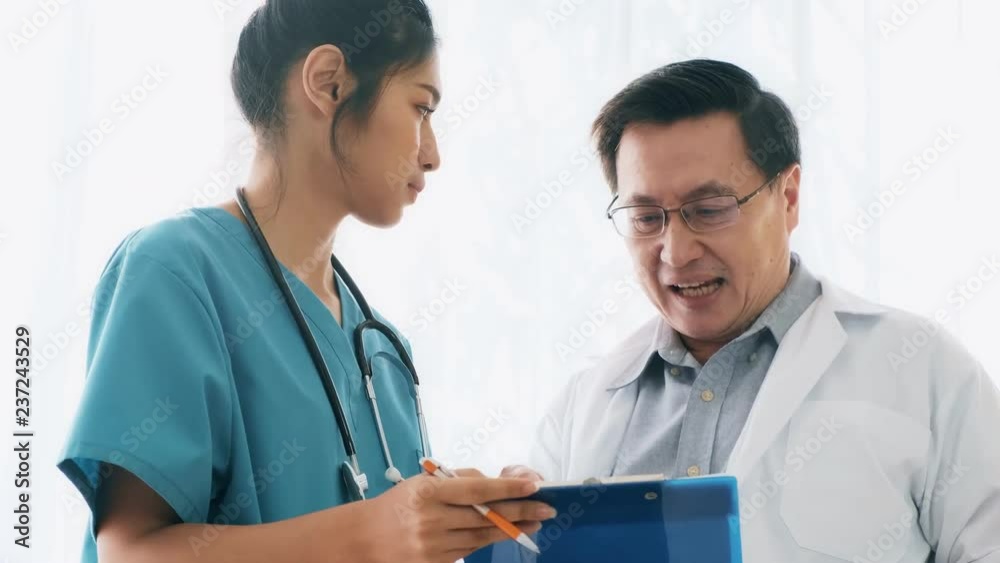 Senior asian man medical doctor standing, talking to young medical woman doctor examine her notes. Young medical doctor career concept. Senior asian man medical doctor standing, talking to young medical woman doctor examine her notes. Young medical doctor career concept.