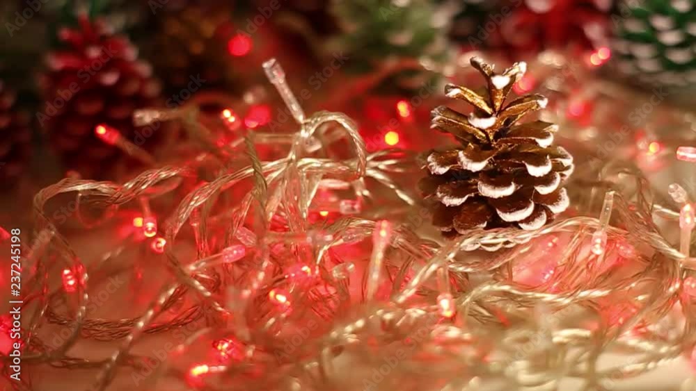 Green, red and brown painted colorful pine cones and led light of Christmas garland glowing ni night darness. Beautiful bright holiday xmas video background. Real time footage.