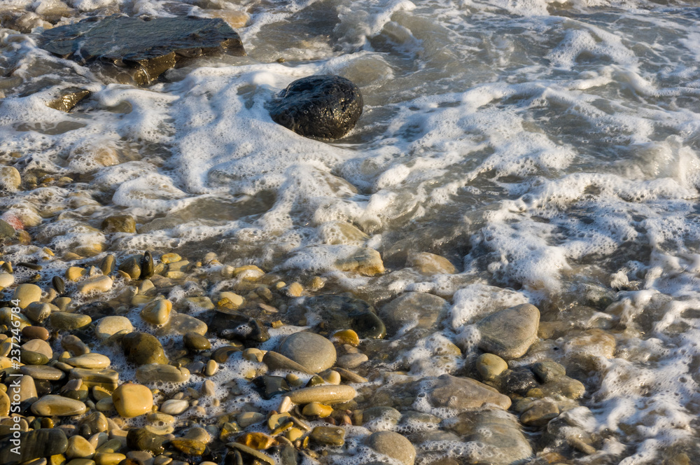 pebble stones on the sea beach, the rolling waves of the sea with foam