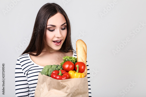 Beautiful woman holding grocery shopping bag on grey background