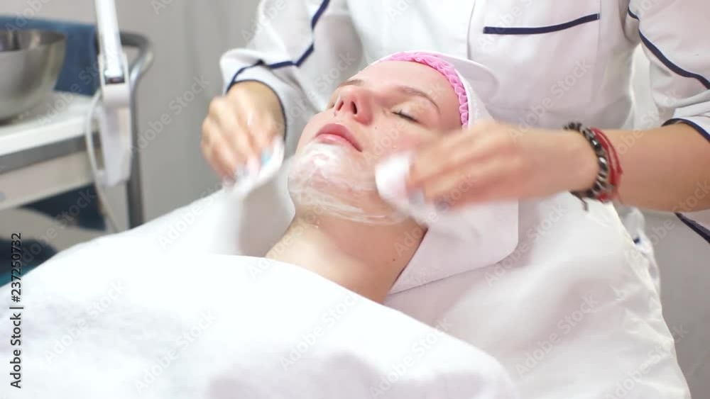 The beautician does the procedure of peeling the skin.young woman in a beauty salon.The beautician spreads the cream on the face of the client.Skin hydration for European girl. The beautician does the procedure of peeling the skin.young woman in a beauty salon.The beautician spreads the cream on the face of the client.Skin hydration for European girl.