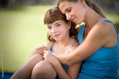 Portrait of a girl being hugged by her mid-adult mother.
