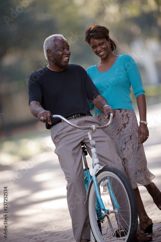 Smiling senior man sitting on a bicycle next to his mid-adult daughter.
