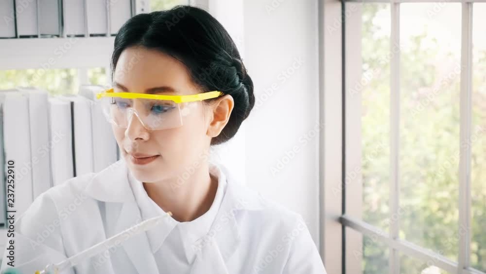 Asian chemist working in a lab. Young female chemist putting chemical liquid in test tube. Science concept. Asian chemist working in a lab. Young female chemist putting chemical liquid in test tube. Science concept.