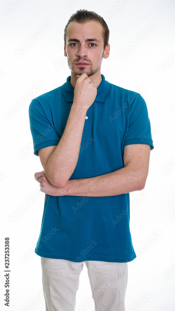 Studio shot of young bearded man standing while thinking against Studio shot of young bearded man standing while thinking against