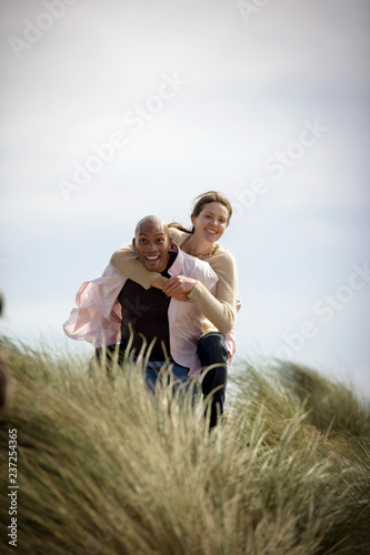 Portrait of a young man giving his wife a piggy-back in between sand dunes. photo