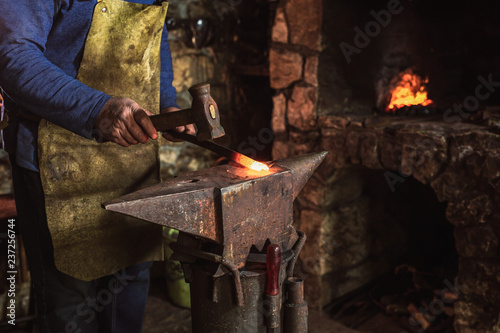 Blacksmith manually forging the molten metal on the anvil in smithy with spark fireworks