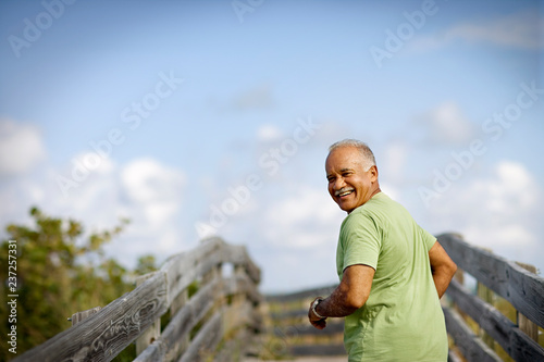 Portrait of a mature adult man smiling as he runs along a wooden beach pathway.