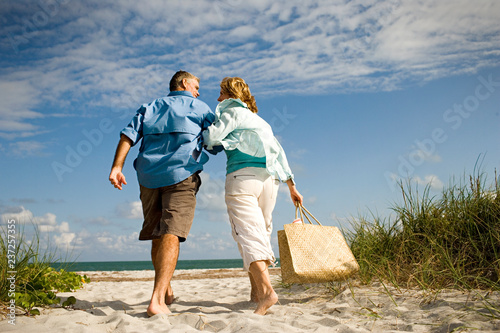 Happy mature couple holding hands while walking together at the beach. photo