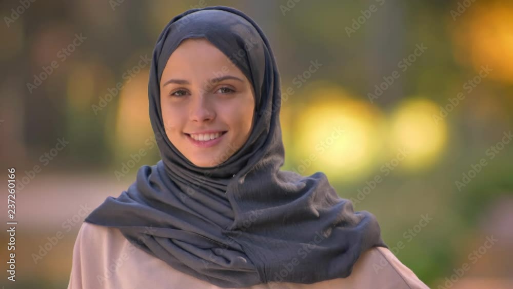 Close-up portrait of Muslim girl in hijab watching into camera, happily nodding to show agreement. Close-up portrait of Muslim girl in hijab watching into camera, happily nodding to show agreement.