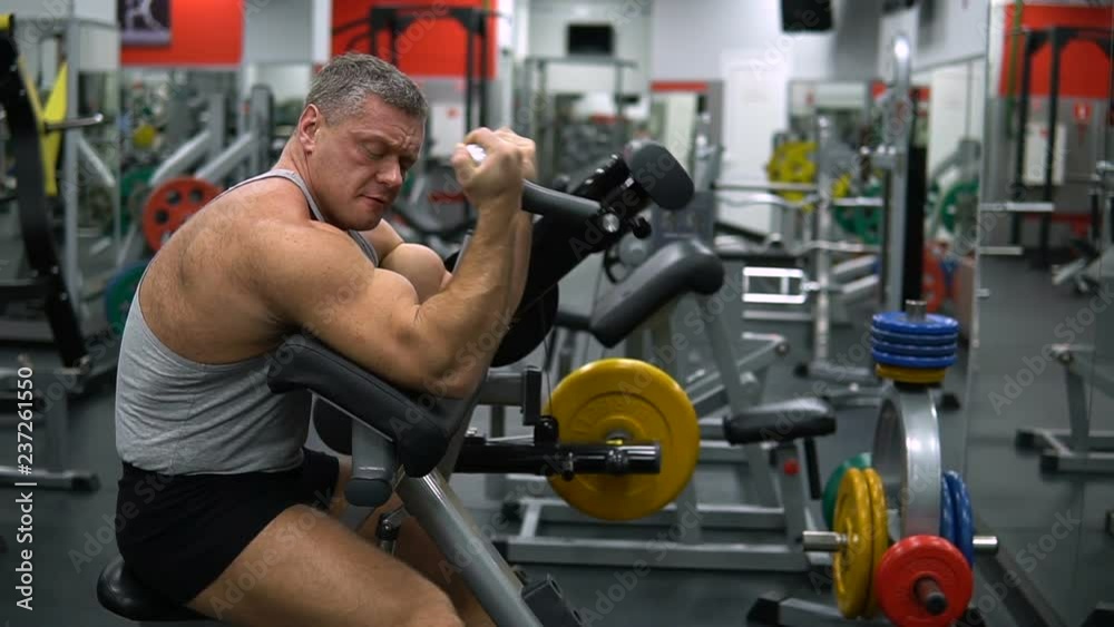 Muscular man trains biceps with a barbell in the gym