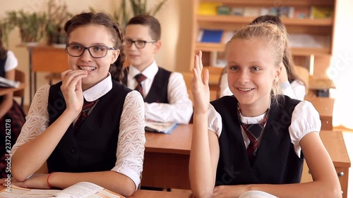 two schoolgirls in uniform at her desk. one pulls the other hand answers the question