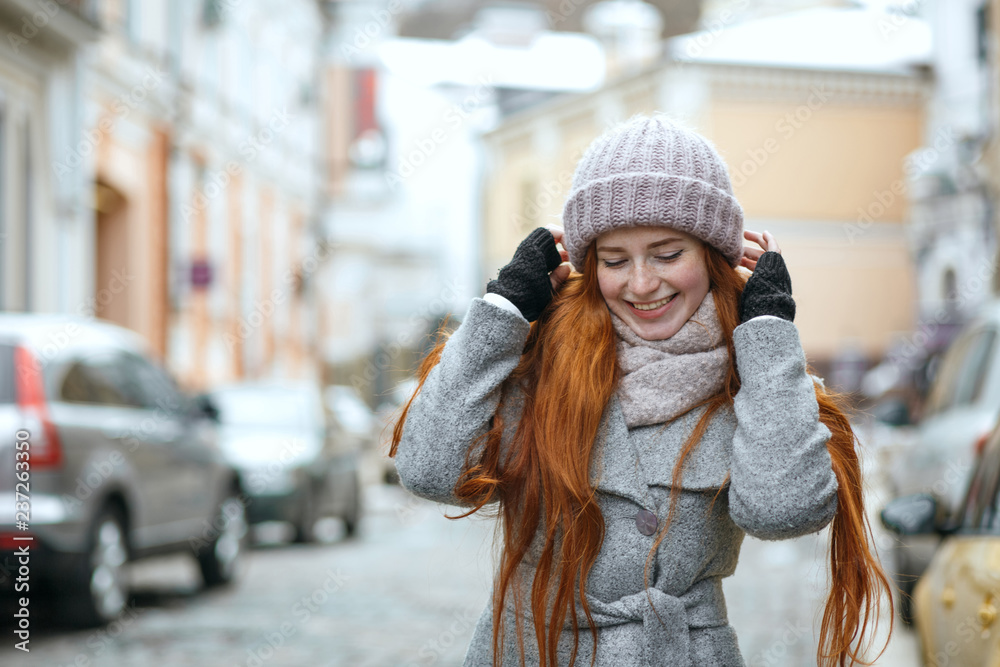 Positive red haired woman wearing warm winter clothes walking down the street. Empty space Positive red haired woman wearing warm winter clothes walking down the street. Empty space