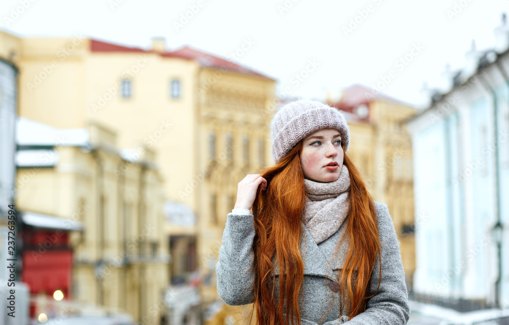 Street portrait of glorious redhead woman with long hair wearing warm winter apparel posing at the street. Empty space Street portrait of glorious redhead woman with long hair wearing warm winter apparel posing at the street. Empty space