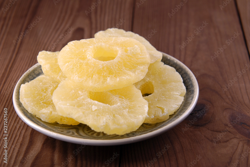 Dry pineapple in sugar on a plate on a brown wooden background. Dry pineapple in sugar on a plate on a brown wooden background.