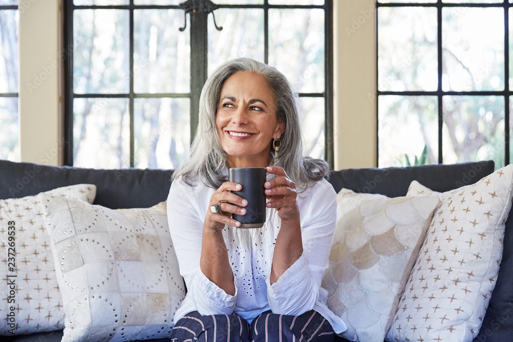Mature woman with grey hair relaxing and drinking tea in her living ...