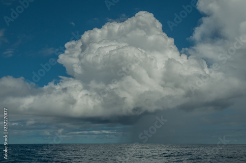 One big fluffy white cloud provides a sudden rain storm on a sunny day at sea.