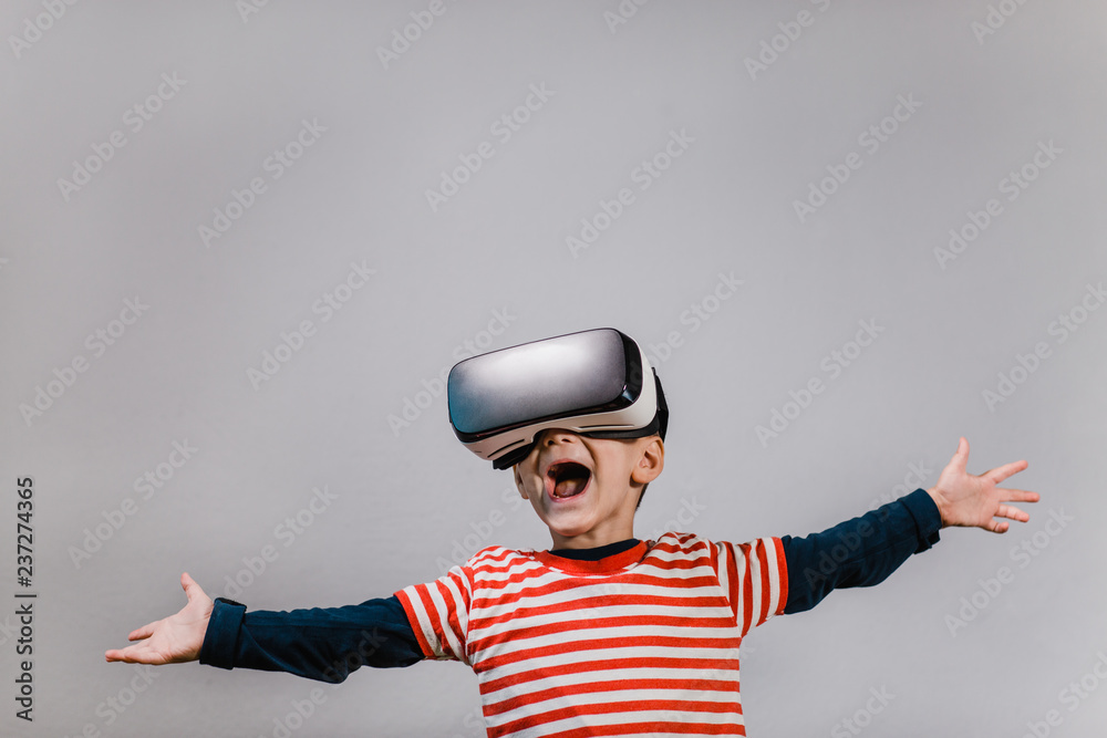 Excited kid with hands spread having fun with VR glasses. Portrait of happy  child wearing virtual reality headset against grey background. Stock Photo  | Adobe Stock