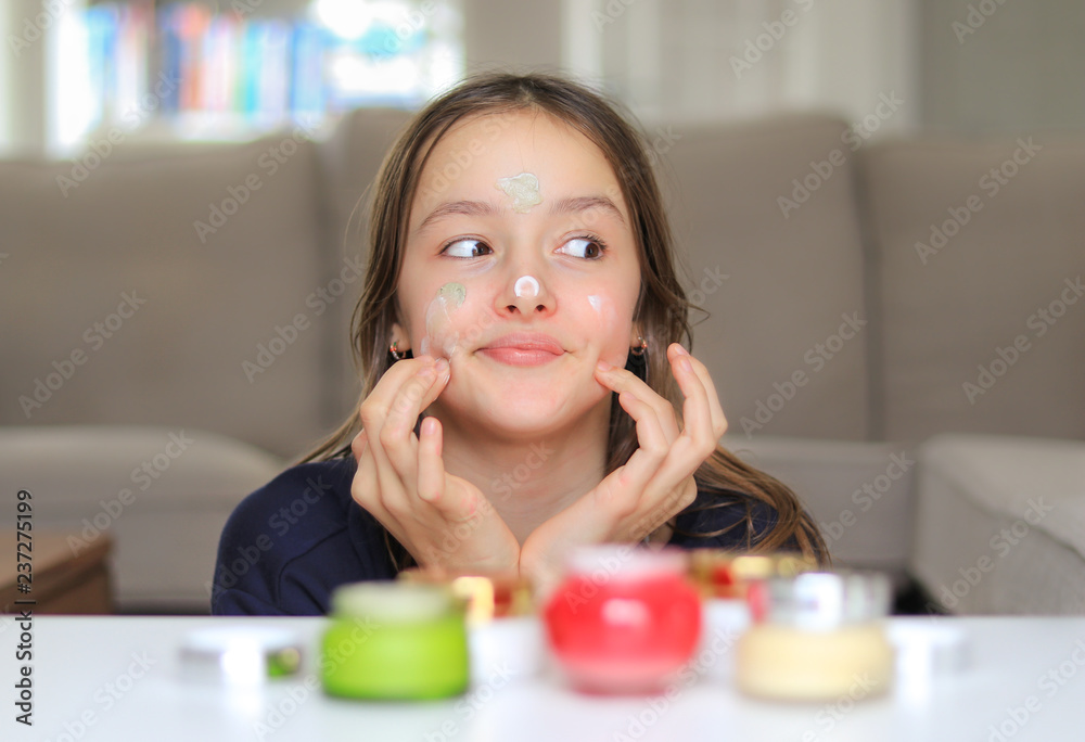 Cute preteen girl applying various cosmetic creams on face skin secretly. Trying first skin care balm. Assortment of treatment for different skin type. Using mother cosmetics