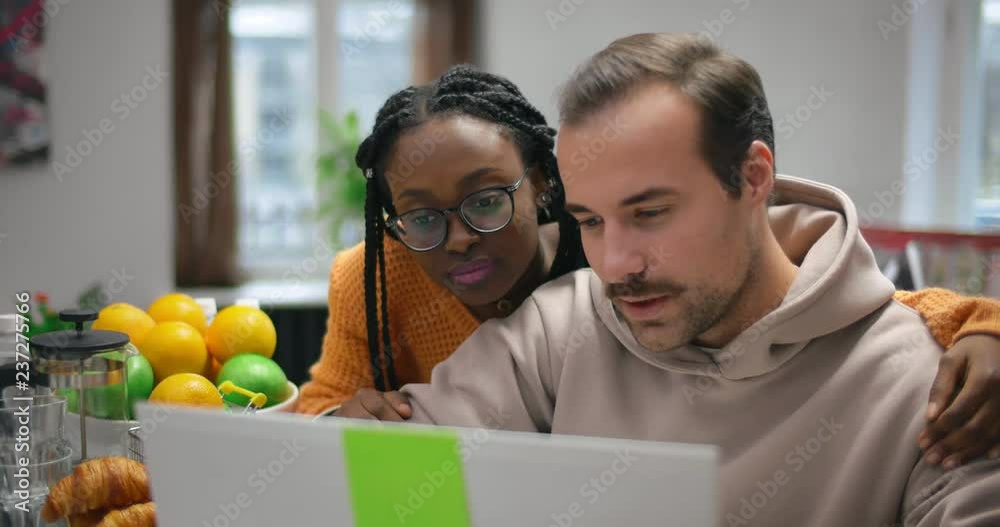 Young multinational couple working together on laptop in a cafe.