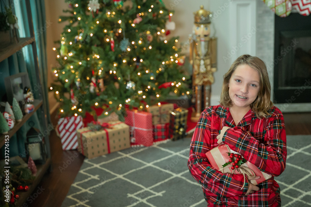 Child Girl Standing Inside In Front of the Christmas Tree Holding a Wrapped Present