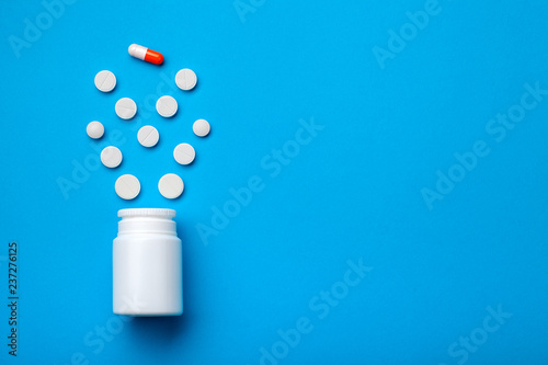 Conceptual background with pills and capsule for treating the gastrointestinal tract and improving appetite, pills on a blue background with a bottle top view.